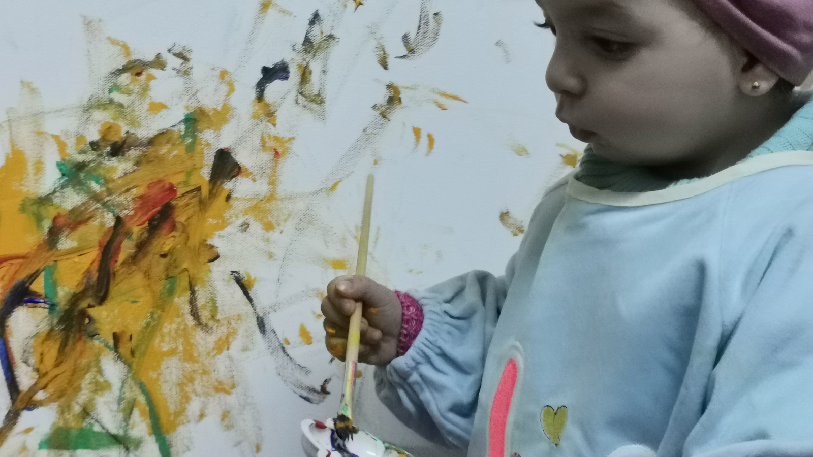 Toddler painting abstract art with a brush on white canvas.